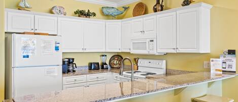 A kitchen with white cabinets, a granite countertop, a refrigerator, a microwave, a stove, and a sink.