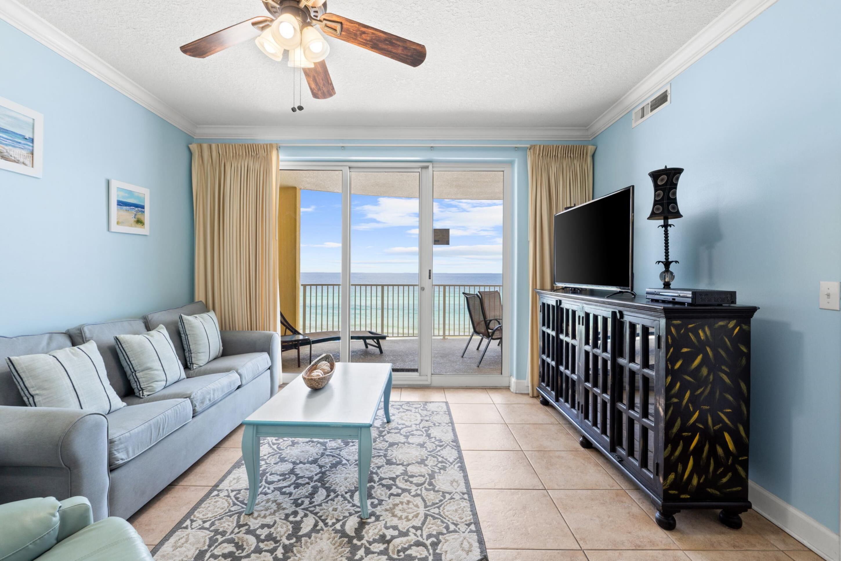 A living room with a sofa, a coffee table, a TV, and a cabinet. There is a balcony with a view of the ocean.