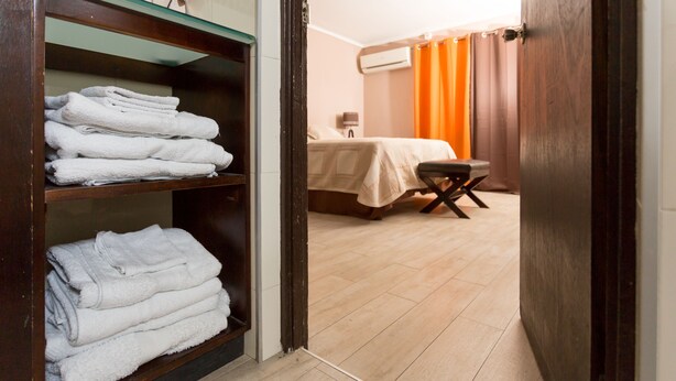 Ein Hotelzimmer mit einem Holzschrank, einem Bett mit orangefarbenem Vorhang und einem kleinen Tisch.