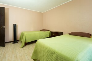 Une chambre avec deux lits, chacun recouvert d’une couverture verte, une table de chevet, une petite table et une grande lampe sur pied.
