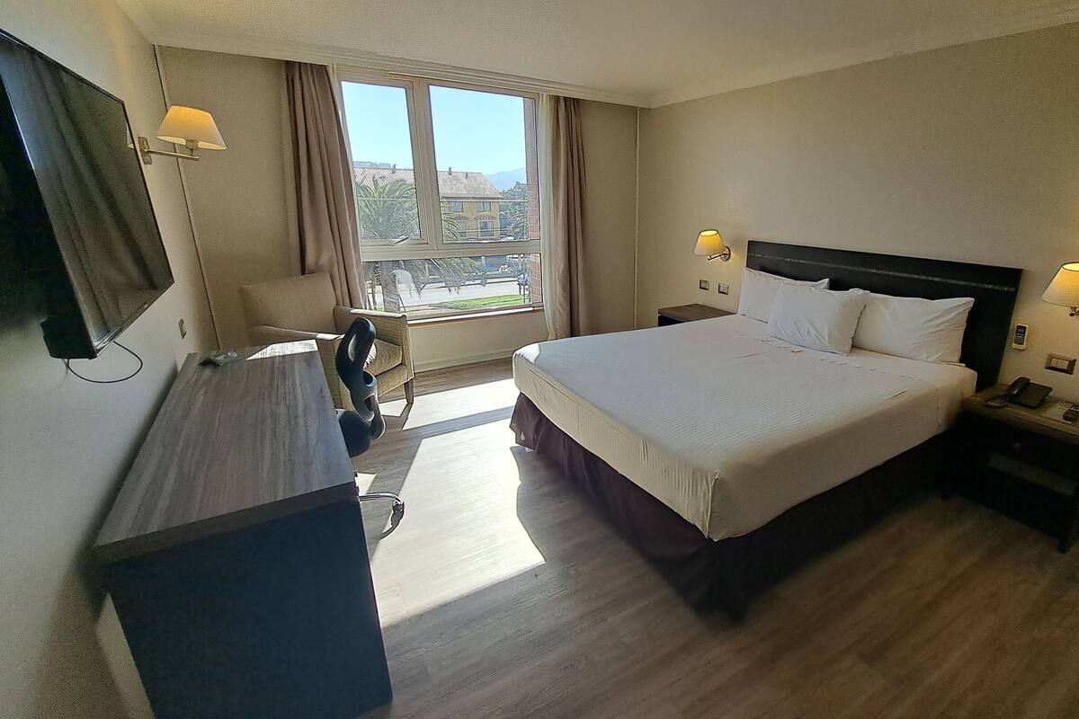 A hotel room with a bed, bedside lamps, a desk, a chair, and a TV.
