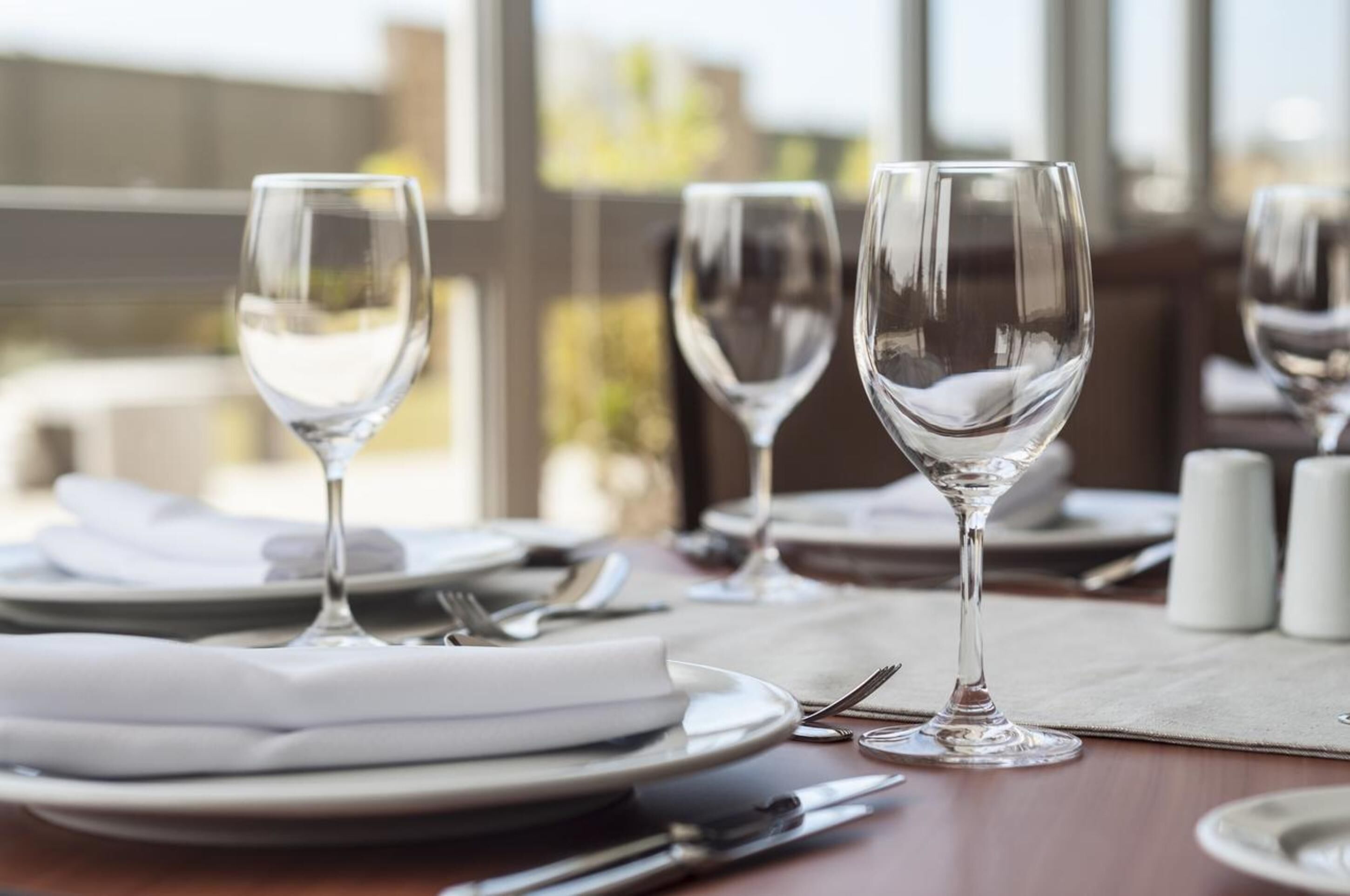 A dining table set with plates, cutlery, and wine glasses, with a view of buildings outside.