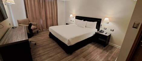A hotel room with a bed, bedside tables, a desk, a chair, and curtains.