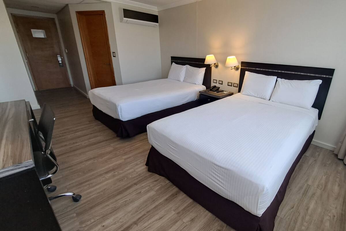 A hotel room with two single beds, a desk with a chair, and a phone on the nightstand.