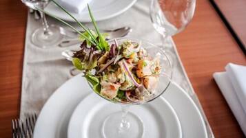 A salad in a glass bowl on a white plate, with a fork and a wine glass in the background.