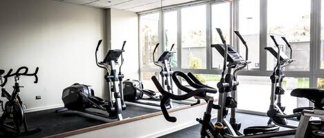 A gym with stationary bikes, treadmills, and a mirrored wall.