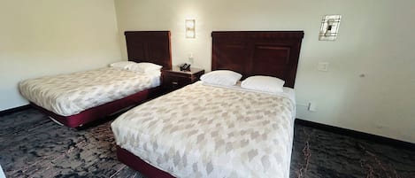 Ein Hotelzimmer mit zwei Betten, einem Holzkopfstück, einem Nachttisch und einer Wandleuchte.