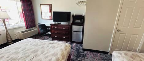 A hotel room with a bed, a desk with a television, a microwave, and a wardrobe.