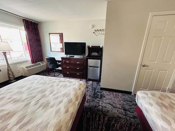 A hotel room with a bed, a desk with a television, a microwave, and a wardrobe. - Economy Inn (Portland)