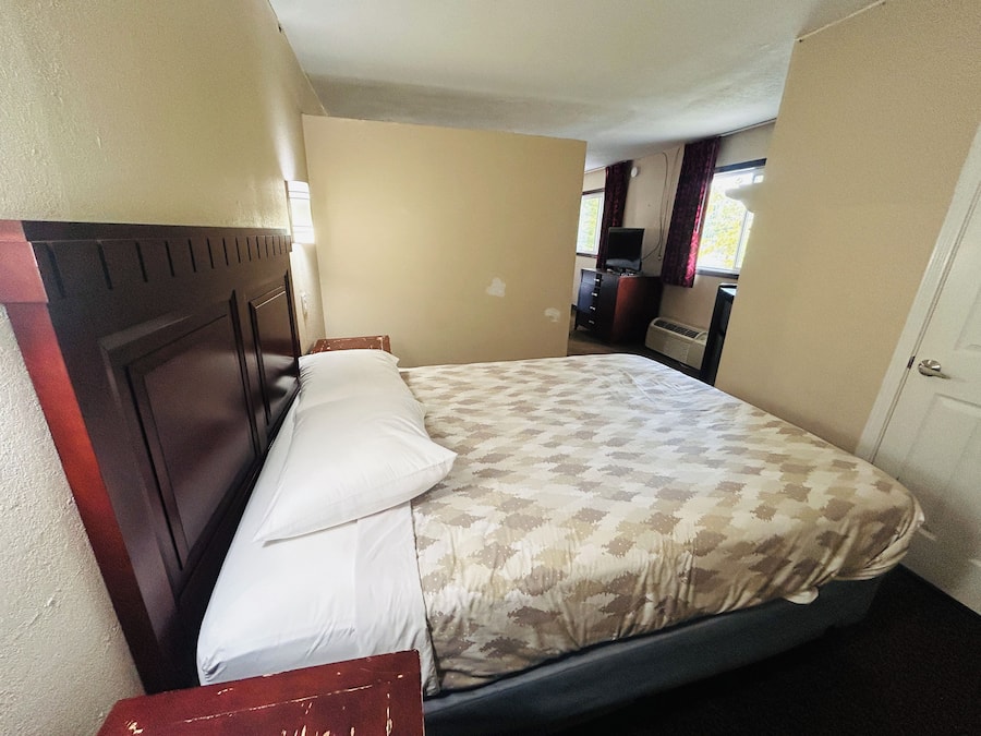 A single bed with a wooden headboard, a bedside table, and a window with curtains.