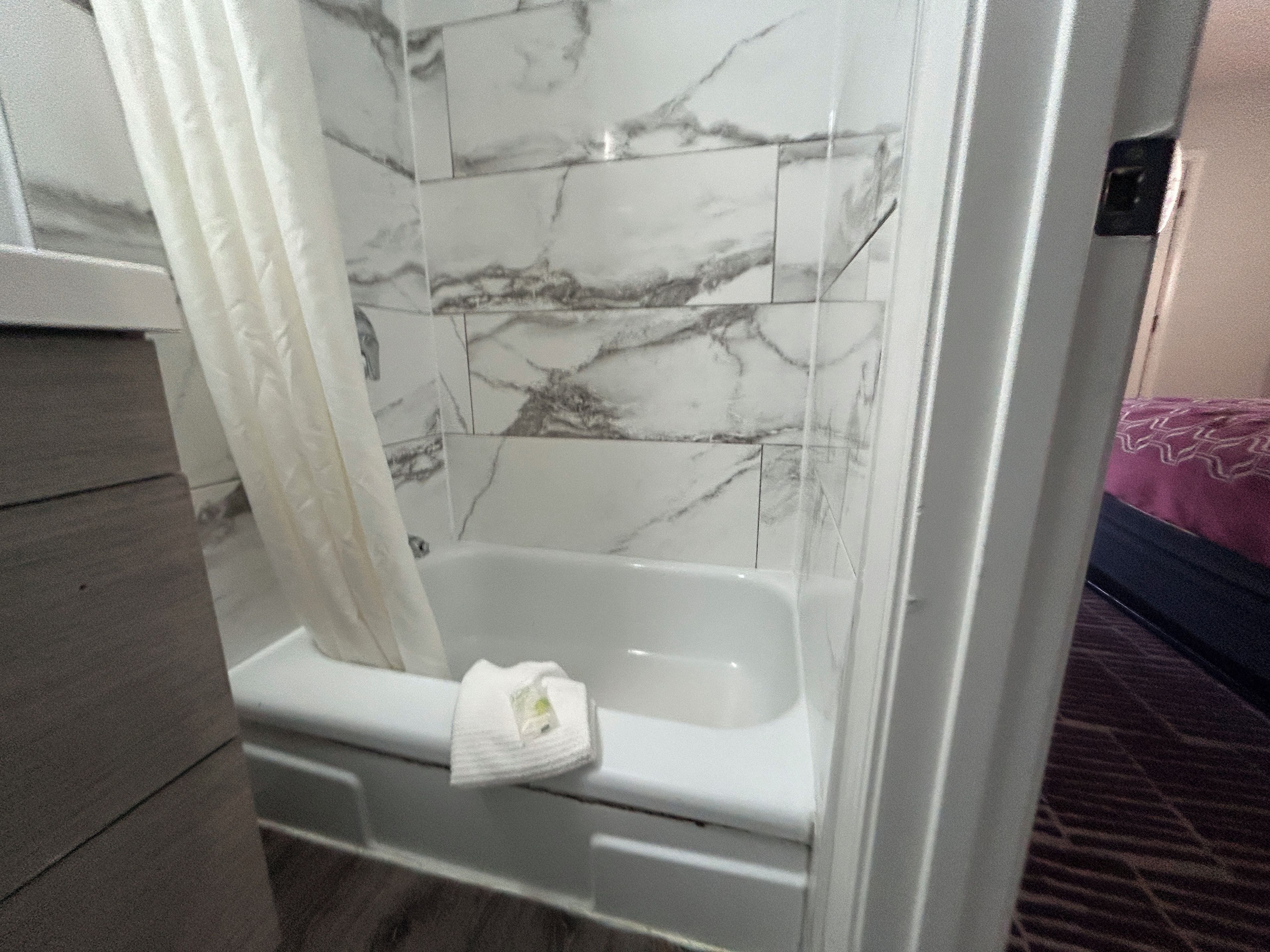 Un baño con bañera, azulejos de mármol y una cortina blanca.