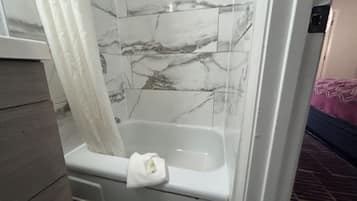 Un baño con bañera, azulejos de mármol y una cortina blanca.