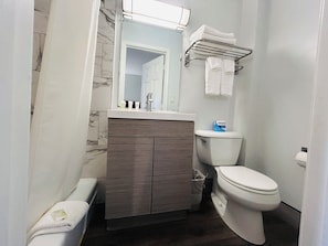 A bathroom with a toilet, a vanity with a mirror, and a towel rack. - Economy Inn (Portland)