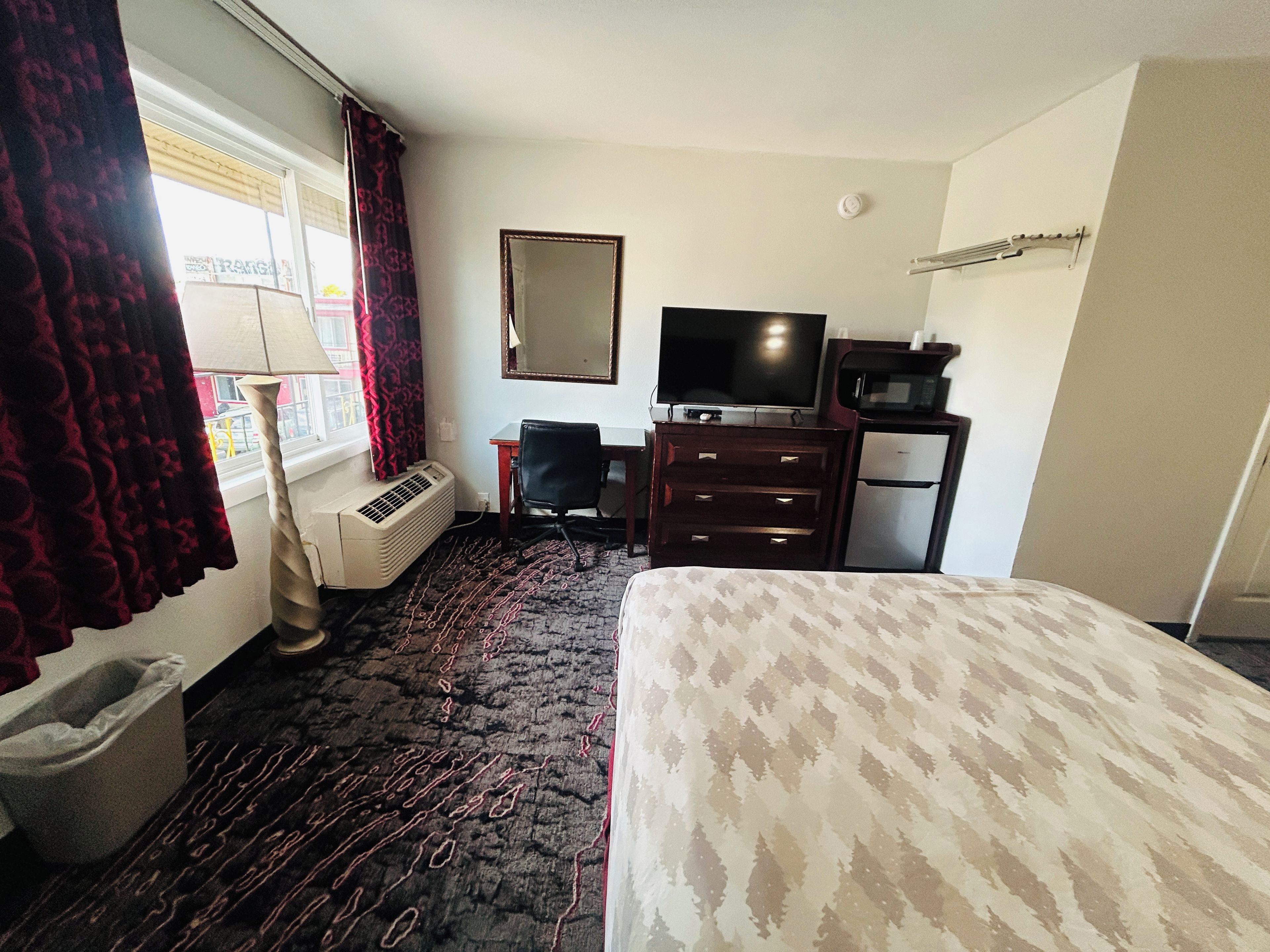 Une chambre d’hôtel équipée d’un lit, d’un bureau, d’une chaise, d’une télévision, d’un four à micro-ondes, d’un radiateur et d’une fenêtre avec des rideaux.