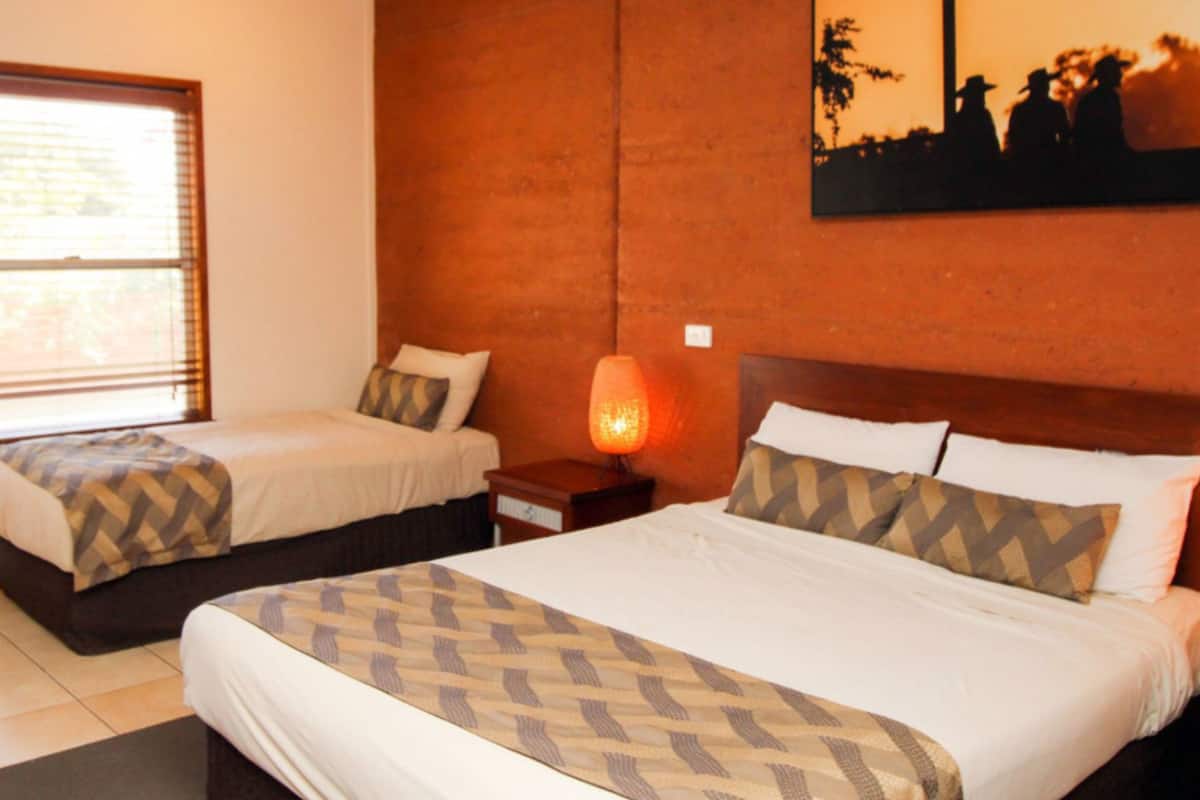 A hotel room with two beds, a nightstand with a lamp, and a wall-mounted painting.