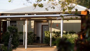 A building with a covered entrance, a door, and a small porch area with a chair. - Gidgee Inn Motel (Cloncurry)