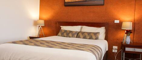 Habitación de hotel con una cama grande, dos mesitas de noche con lámparas, un cuadro en la pared y una mesita con un jarrón.