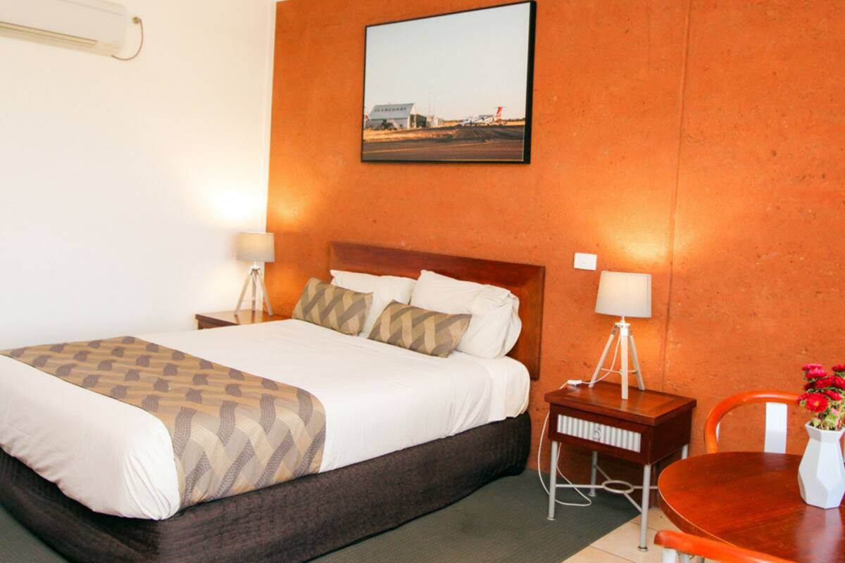 A hotel room with a large bed, two bedside lamps, a wooden nightstand, a small table with a vase of flowers, and a framed picture on the wall.