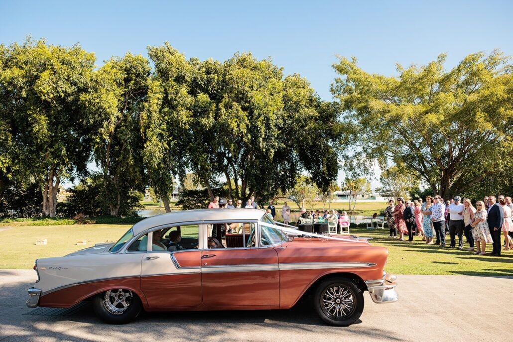 A vintage car parked in a park with a crowd of people in the background.