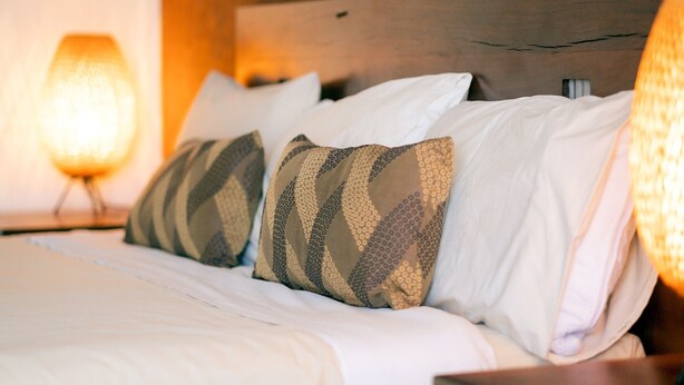 A neatly made bed with patterned pillows and a wooden headboard. - Gidgee Inn Motel (Cloncurry)