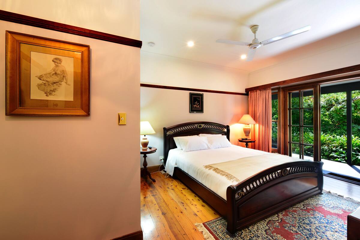 Une chambre avec un grand lit, un ventilateur de plafond, une table de chevet avec une lampe et un tableau encadré au mur.