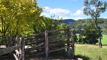 Una valla de madera rústica en un entorno rural, con un cielo despejado y campos verdes al fondo.