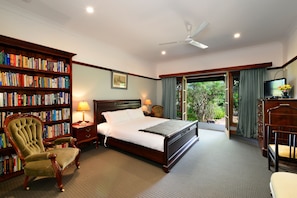 A bedroom with a large bed, a wooden bookshelf, a chair, a desk, and a television.