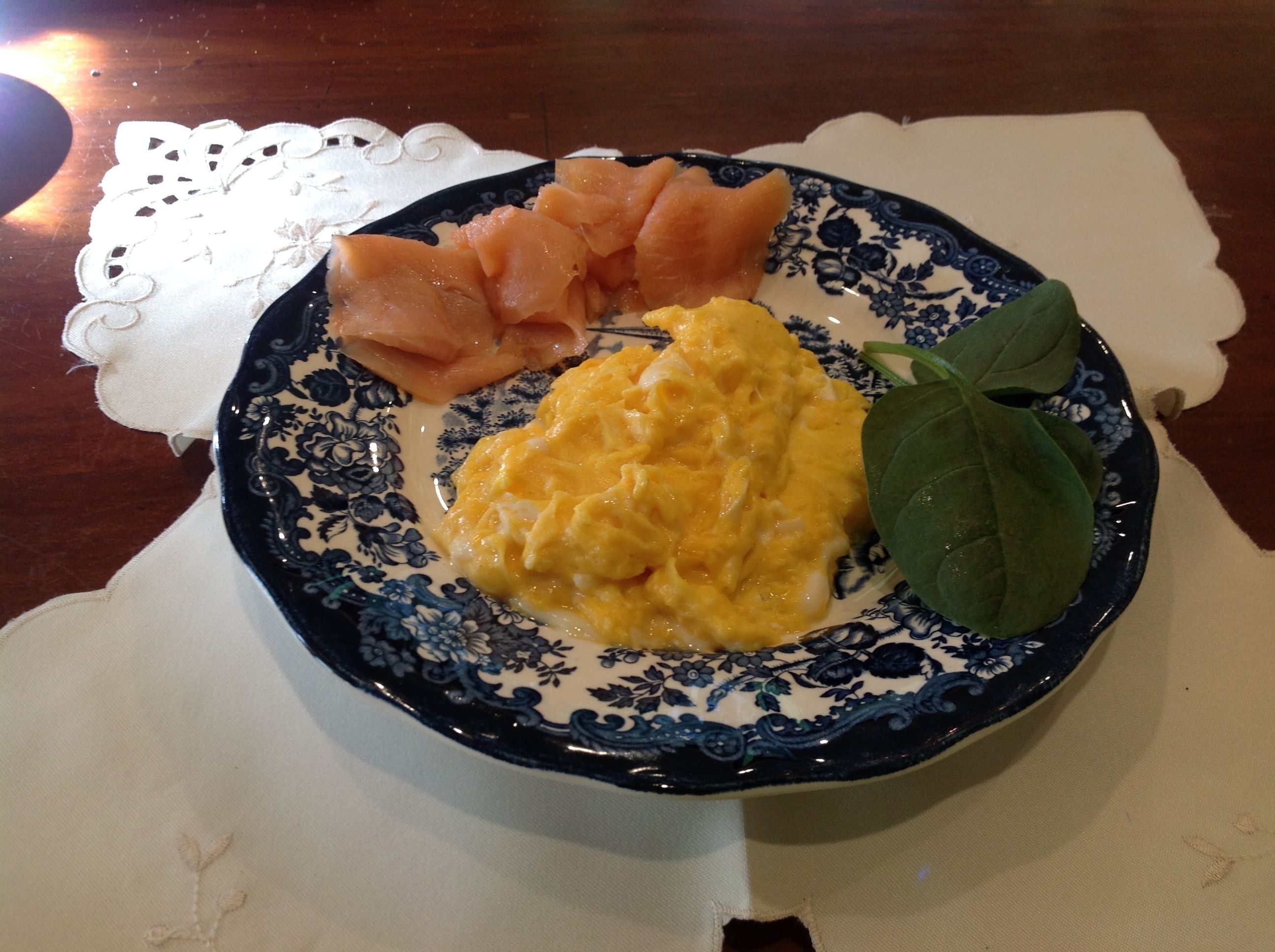 A plate with scrambled eggs, smoked salmon, and a spinach leaf on a blue and white patterned plate.