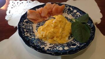 A plate with scrambled eggs, smoked salmon, and a spinach leaf on a blue and white patterned plate.