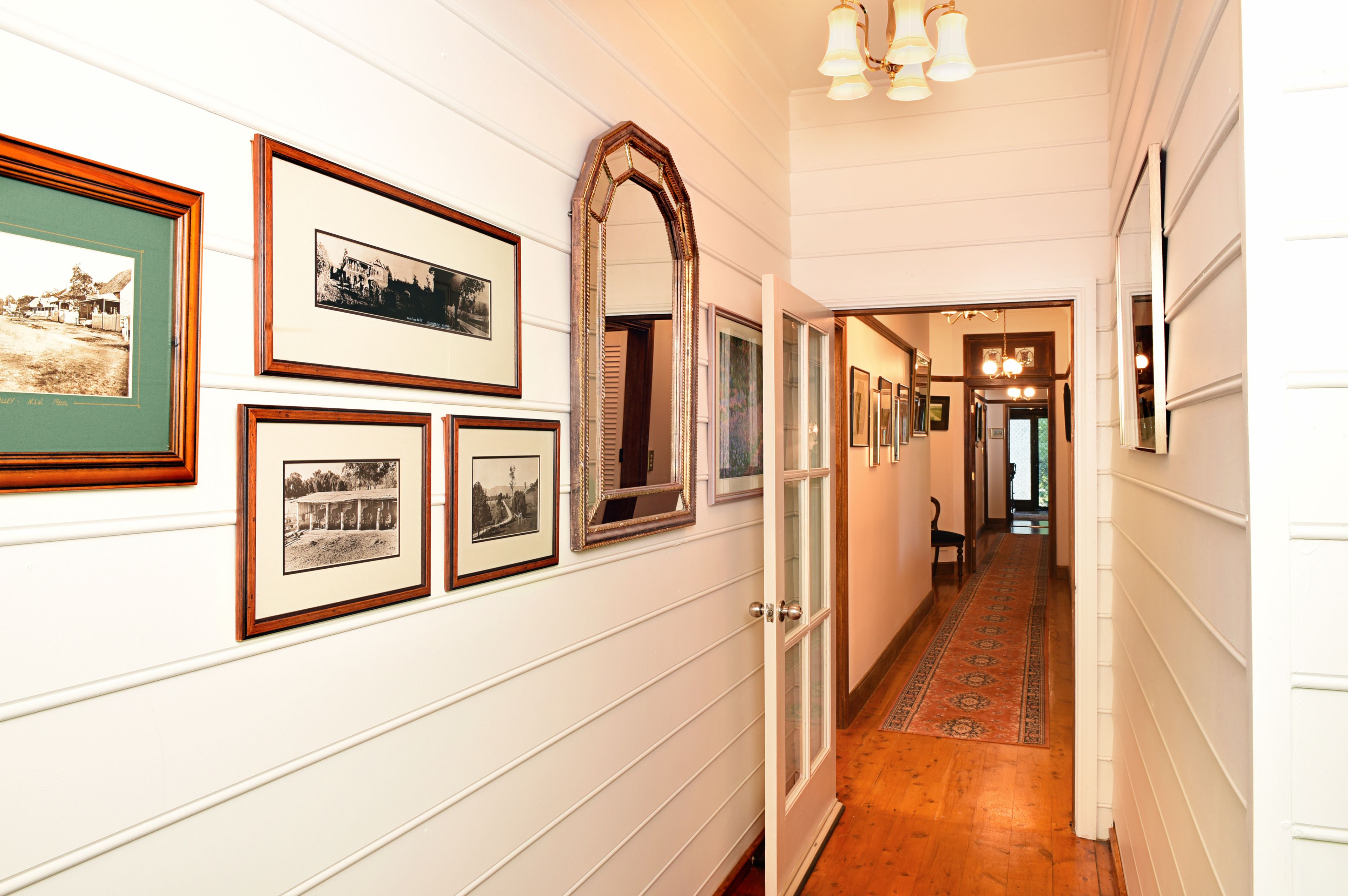 A hallway with framed photographs on the walls, a mirror, and a patterned carpet.