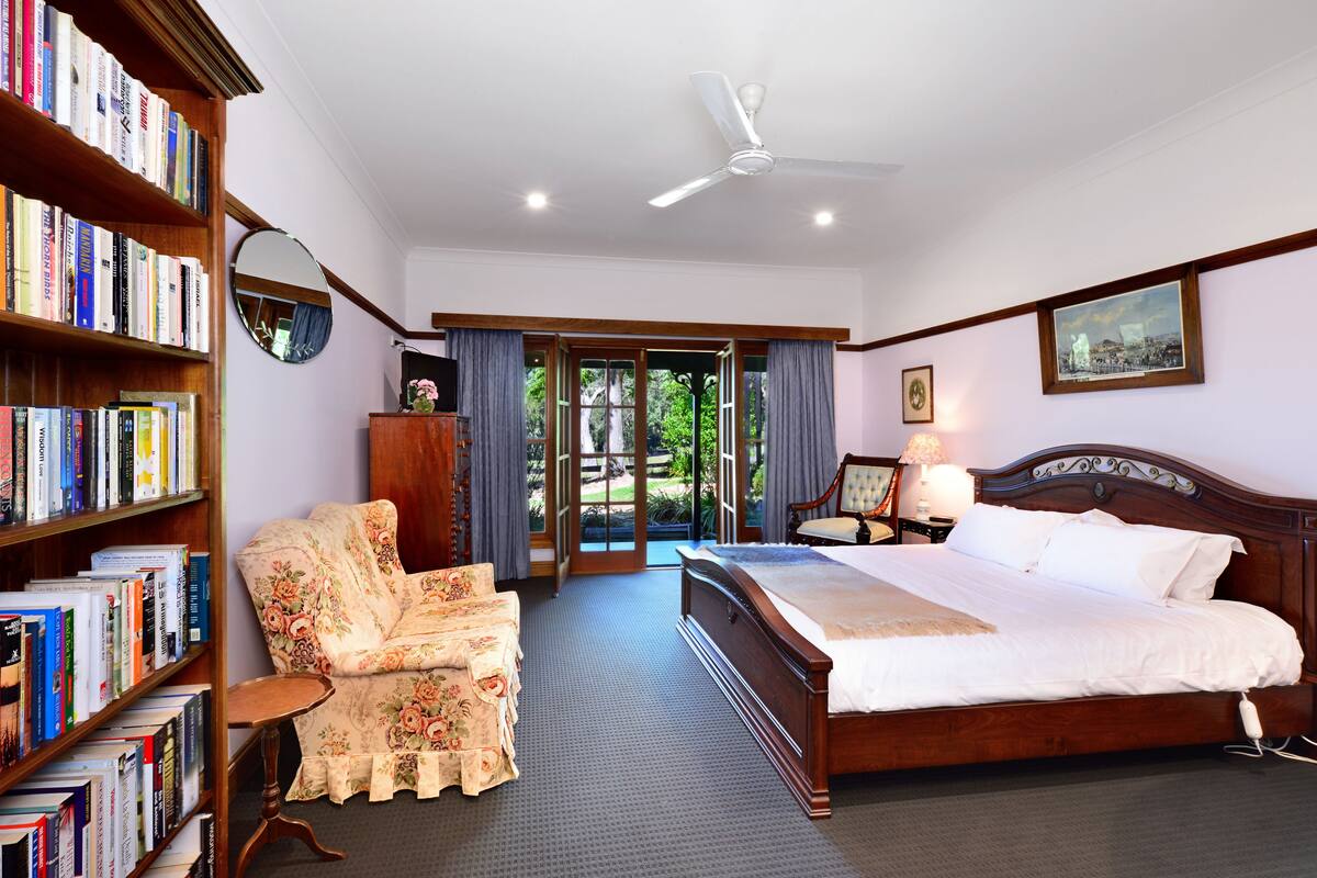 Une chambre avec un grand lit, une chaise, une bibliothèque et une vue à travers une porte vitrée.