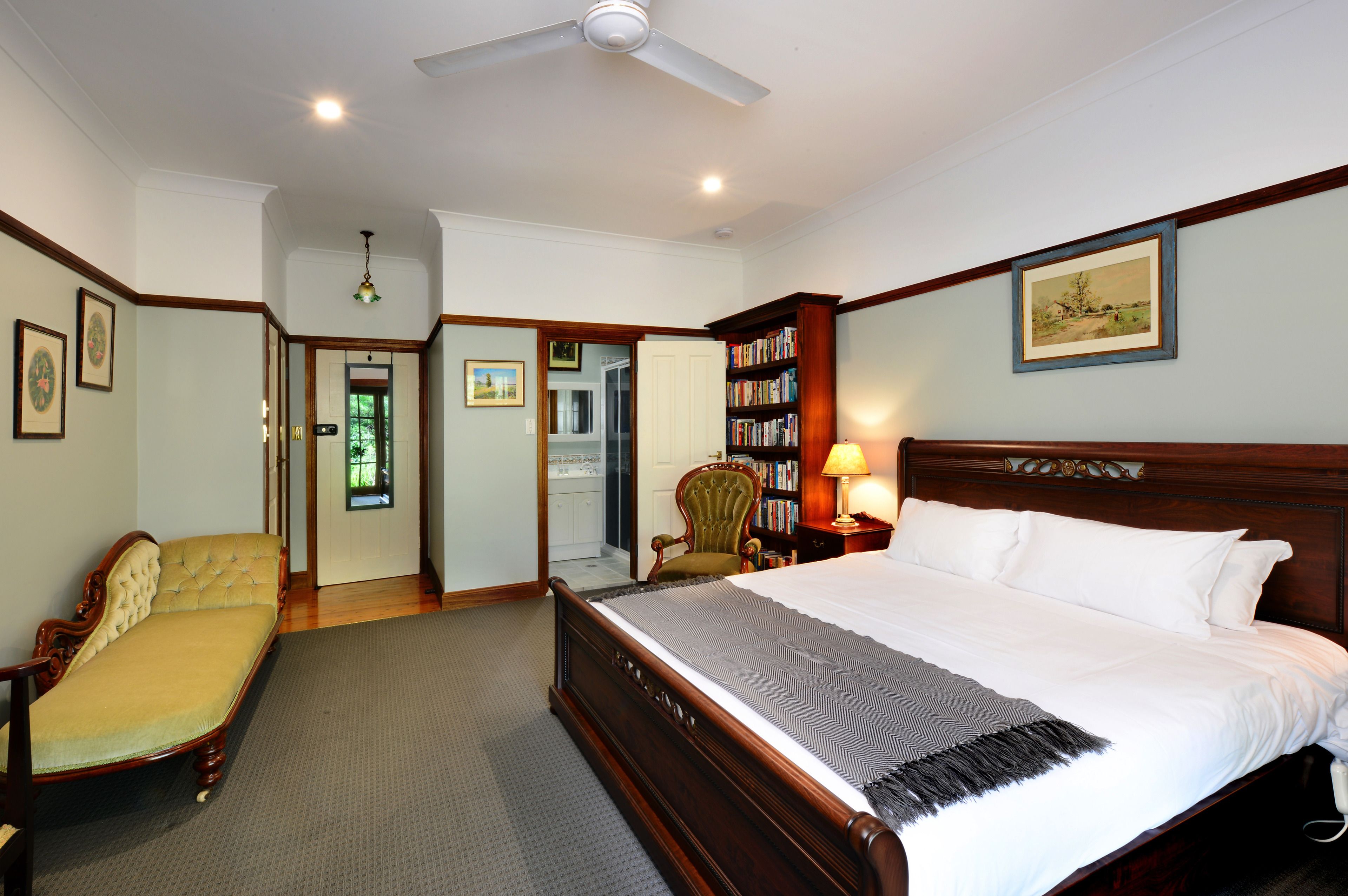 Un dormitorio con una cama grande, una silla, una estantería y una puerta que da a otra habitación.