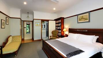 A bedroom with a large bed, a chair, a bookshelf, and a door leading to another room.