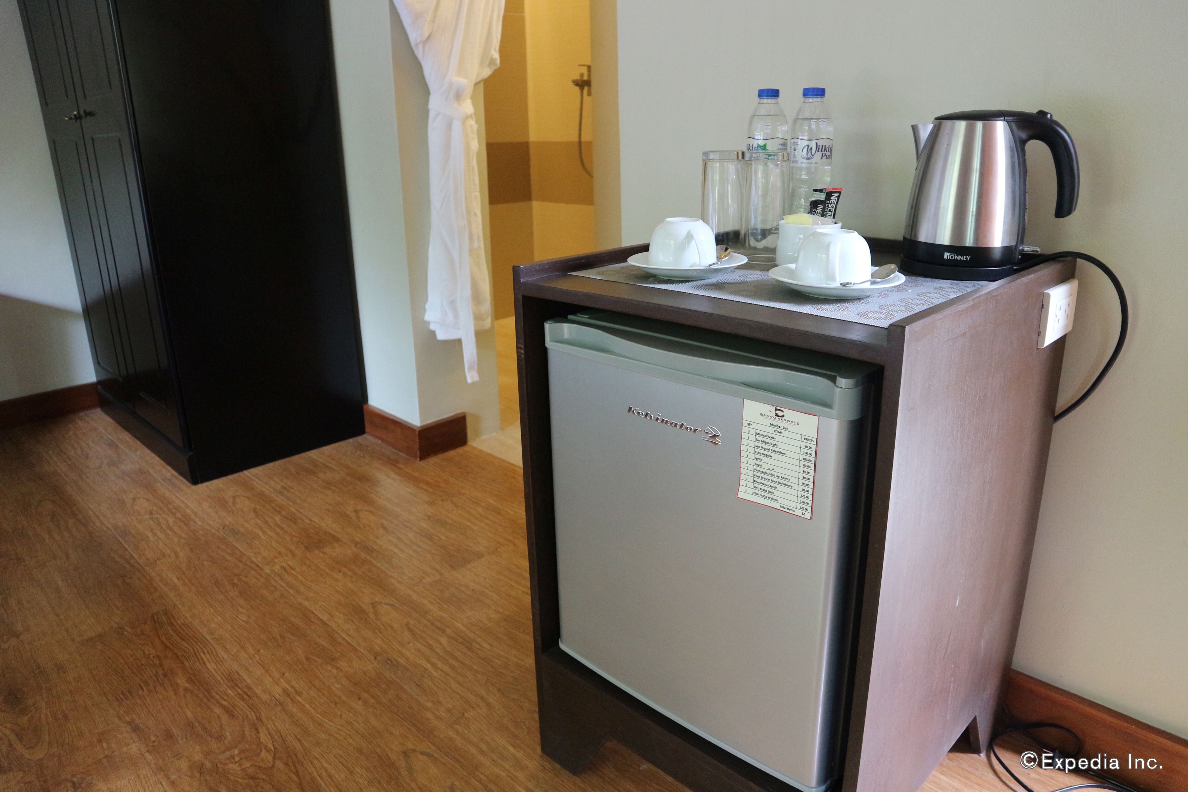 Un minibar compacto con refrigerador, cafetera y una botella de agua.