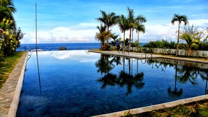 Ein unendlicher Pool mit klarem Wasser, umgeben von Palmen und einer Steinmauer, der Himmel und Palmen darin widergespiegelt werden.