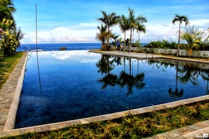 Ein unendlicher Pool mit klarem Wasser, umgeben von Palmen und einer Steinmauer, der Himmel und Palmen darin widergespiegelt werden.