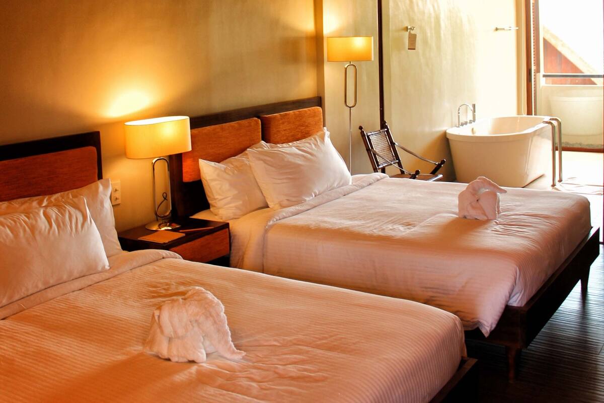 Ein Hotelzimmer mit zwei Betten, einem Deckenventilator, einem großen Fenster und einer Badewanne.