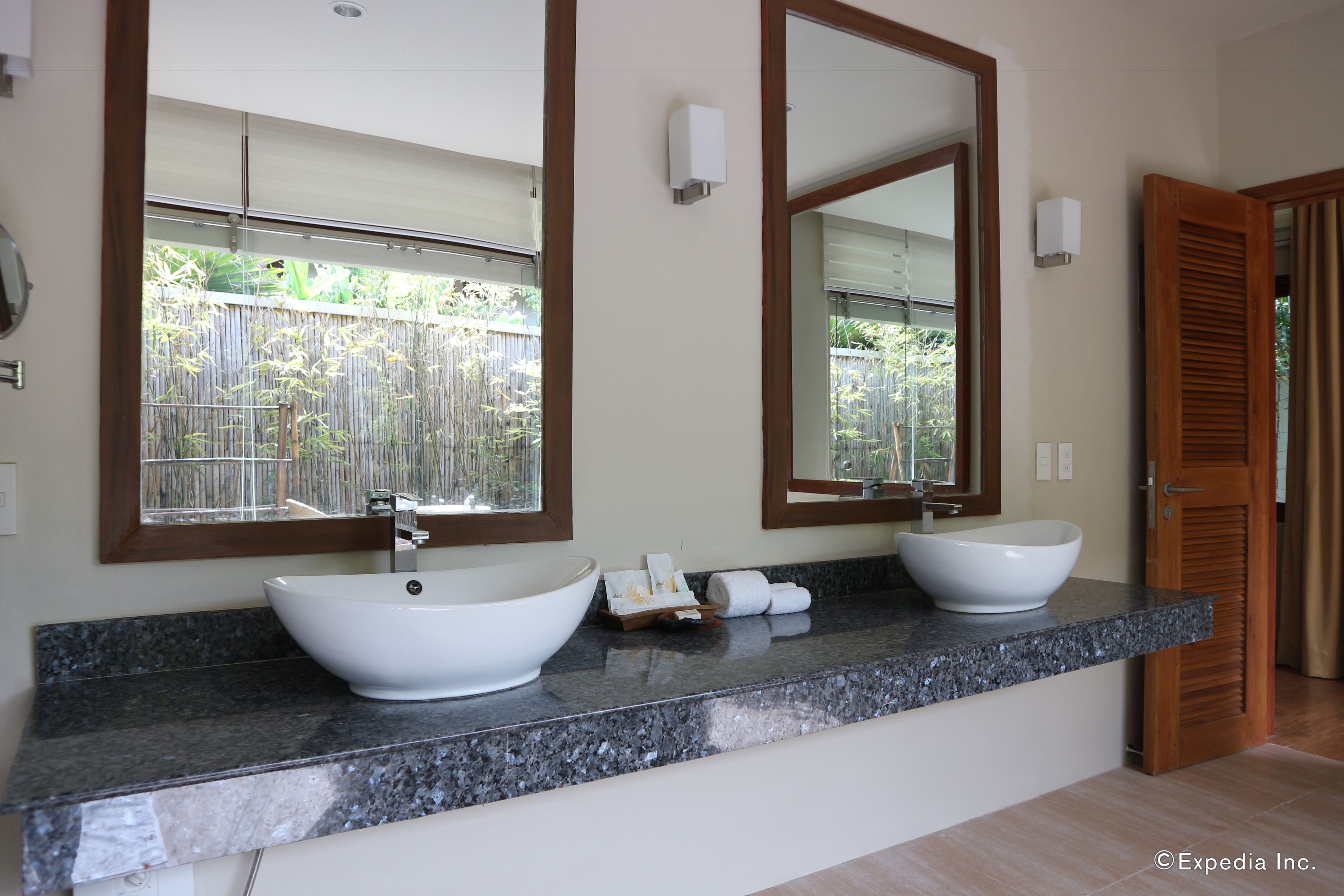 Un baño con dos lavamanos tipo recipiente, un espejo grande y una puerta de madera.