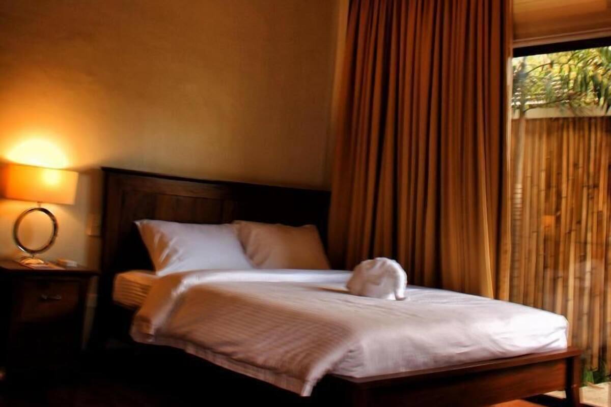 Ein ordentlich bezogenes Bett mit weißer Bettdecke und Kissen, einer Nachttischlampe und einem Holzkopfende.