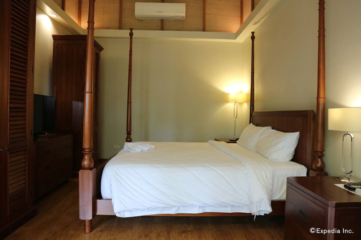 Ein Himmelbett mit weißer Bettwäsche, einem Holz-Kopfteil und Nachttischen mit Lampen.
