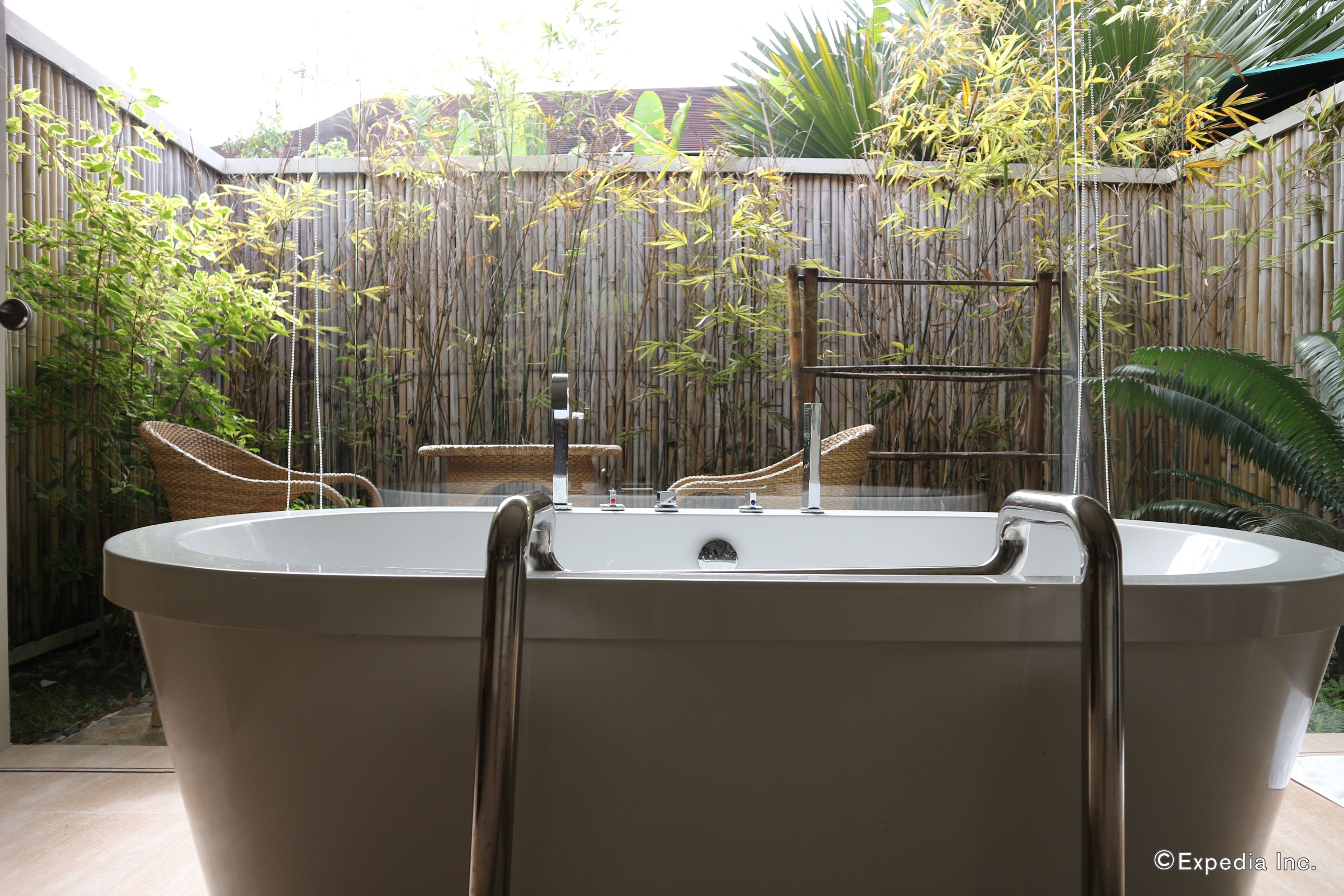 Une baignoire sur pied, entourée d’une paroi en verre, de plantes en bambou et d’une clôture en bois.