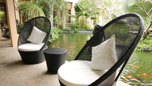 Two wicker lounge chairs with white cushions on a stone patio with a koi pond in the background. - Bravo Resorts - Munting Paraiso (Dauin)