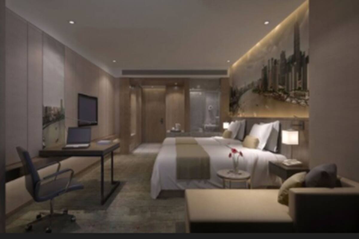 Habitació d'hotel moderna amb un llit, un escriptori amb un ordinador portàtil, una cadira, una taula petita amb una làmpada i un gran finestral amb vista a la ciutat.