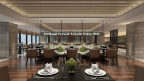 A modern dining area with multiple tables set for service, featuring a central chandelier and a view of the cityscape through large windows. - Shanghai Pudong Theme Park Wassim Hotel (Shanghai)