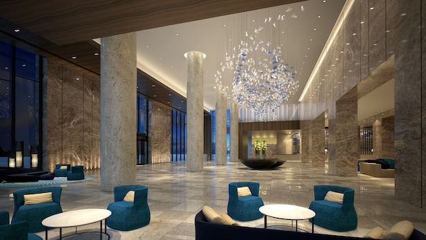 A spacious lobby with high ceilings, marble columns, and a central chandelier. There are seating areas with blue chairs and a large, round table. - Shanghai Pudong Theme Park Wassim Hotel (Shanghai)