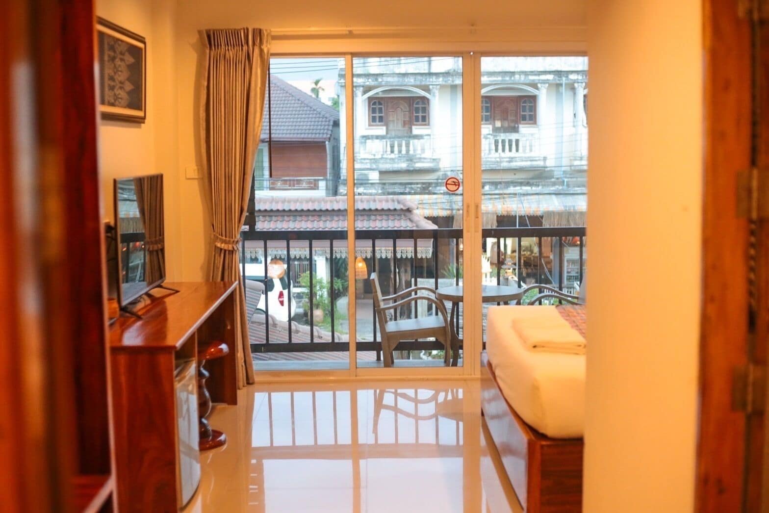 A room with a balcony, a bed, a TV, and a wooden cabinet.