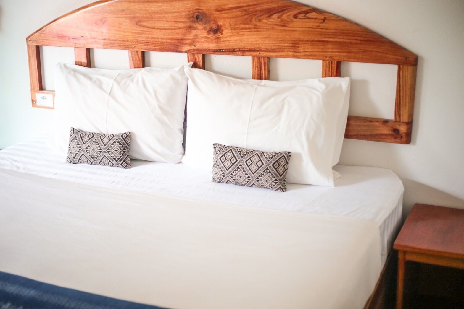 Una cama con cabecera de madera, ropa de cama blanca y dos almohadas estampadas.