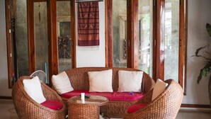 A wicker sofa set with cushions, a glass coffee table, and a fan. - Baan Krittika (Udon Thani)