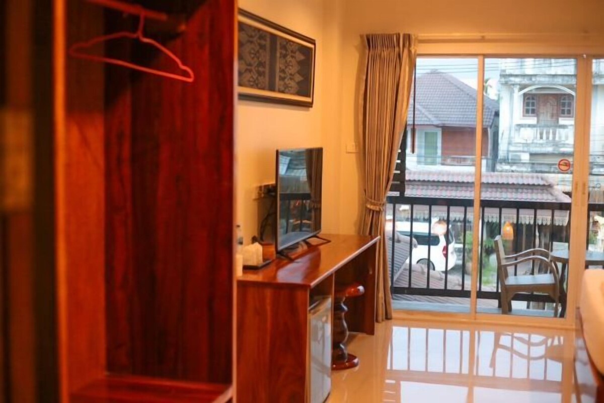 Una habitación con un armario de madera, televisor y balcón con vistas a edificios y un coche.