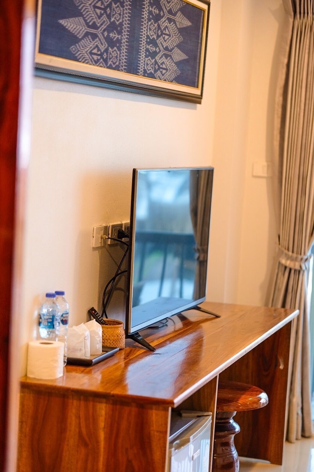 A wooden TV stand with a flat-screen TV, a framed picture above, and a water bottle on the left.